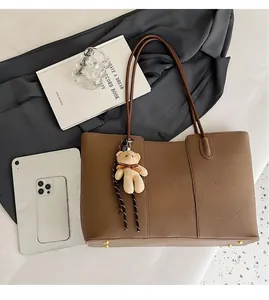 Flat lay of brown lychee grain tote bag with plush bear charm and golden protective feet