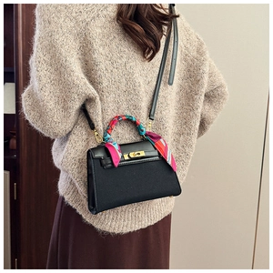 Detail of black leather handbag with decorative silk scarf handle and golden metal lock