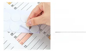 Close-up showing a hand peeling a round double-sided adhesive dot for 2026 calendars