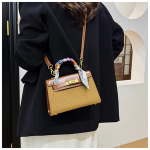 Detail of a brown leather crossbody bag with a decorative silk scarf on the handle