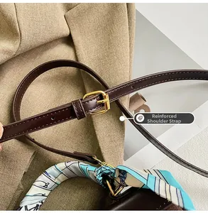 Close-up of brown leather bag with reinforced strap, gold buckle, and patterned silk scarf