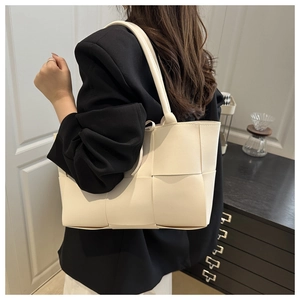 Détail d'un sac seau tressé beige porté par un mannequin dans un cadre minimaliste