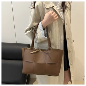 Détail d'un sac seau tressé marron porté par un mannequin en trench-coat beige élégant et moderne