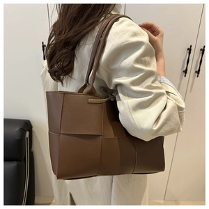 Détail du sac seau tressé marron foncé montrant l'artisanat du cuir à larges lanières