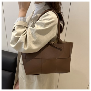 Détail d'un grand sac seau tressé marron foncé porté avec un trench-coat beige