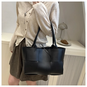 Détail du sac cabas tissé noir avec nœud sur le mannequin dans un décor intérieur
