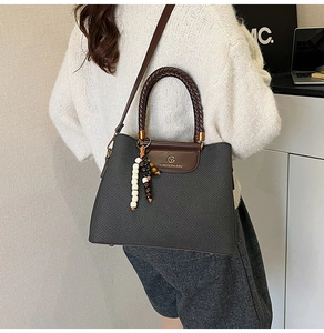 Detail der grauen Stofftasche mit gewebten Rundgriffen und einem Perlen-Quastenanhänger