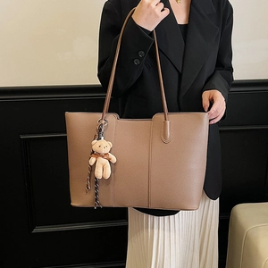 Brown large capacity leather tote bag with cute bear charm worn by a model