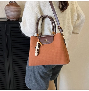 Detailaufnahme der gewebten Textur der karamellbraunen Handtasche mit Perlenanhänger
