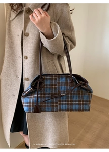 Detail of plaid wool tote bag with leather handles shown on shoulder with wool coat