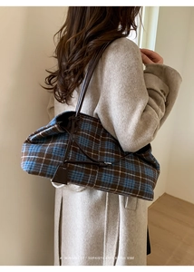 Detail of blue plaid wool tote bag with slim leather straps worn over a beige coat