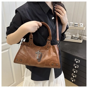 Close-up of brown vintage leather bag with silver cross pendant and rivet accents