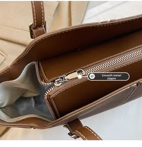 Detail eines glatten Metallreißverschlusses und strukturierten Leders an einem braunen Shopper
