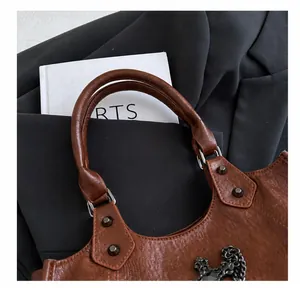 Detail of brown lychee texture leather bag with metal rivets and retro cross pendant