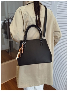 Detail of black lychee grain leather tote bag with ethnic bead tassel and adjustable strap