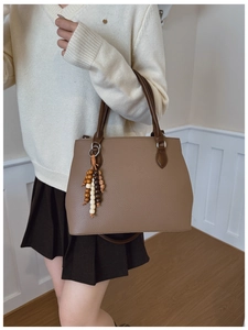 Detail of taupe pebbled leather tote bag with wooden bead charm and brown handle