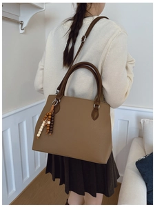 Brown leather tote bag detail with lychee texture, round handles and beaded pendant charm