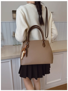 Detail of brown litchi pattern leather tote bag with beaded tassel charm and dual handles