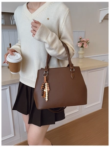 Brown litchi-grain leather tote bag with wooden bead tassel in a lifestyle setting