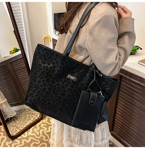 Detail der schwarzen Tote-Bag mit Leopardenmuster, Metallplakette und kleiner Münztasche