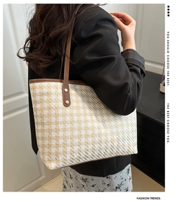 Detail of checkered woven tote with brown leather handles and golden rivet accents