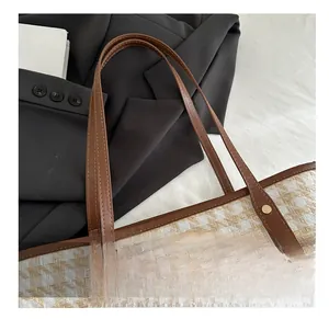 Close-up of woven tote bag with brown leather handle and gold rivet reinforcement