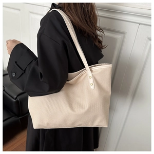 Beige woven tote bag with long shoulder straps shown on model in black coat