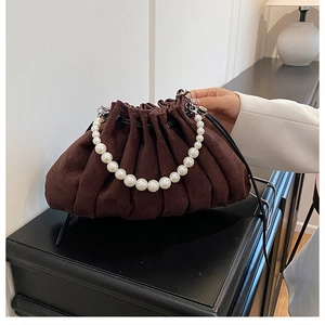 Detail of coffee suede pleated handbag with elegant pearl handle on a wooden table