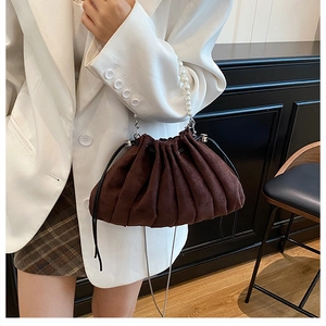 Brown pleated bucket bag with pearl handle and metal chain shown on a model