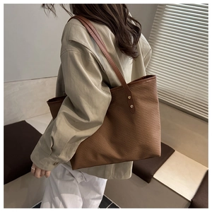 Detail of dark brown woven tote bag with leather straps on model in warm home setting