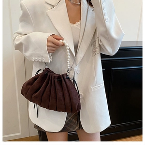 Detail of dark brown ruched drawstring bag with pearl handle and metal strap on model