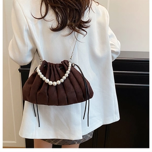 Detail of a pleated dark brown suede bucket bag with large pearl handle and metal chain strap