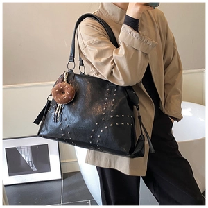 Detail view of large black tote bag with silver rivets and a donut plush pendant