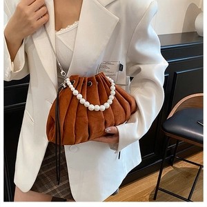 Detail of caramel pleated bucket bag featuring pearl handle and metallic chain strap