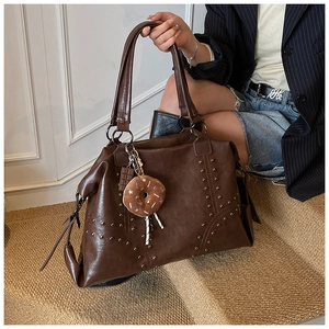 Close-up of brown studded tote bag with donut pendant charm and large storage space