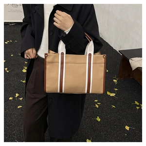 Outdoor view of khaki canvas tote bag with brown leather trim and white handles