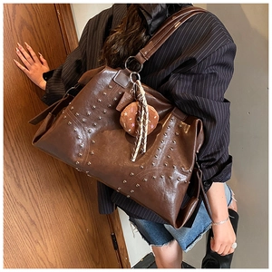 Detail of a large brown leather tote bag featuring silver studs and a plush star charm