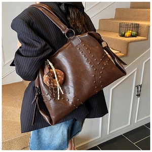 Detail of dark brown rivet tote bag with soft leather texture and stylish doll charm
