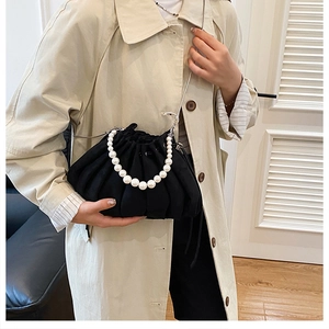 Detail of black pleated pouch bag featuring large pearl handle and metal chain strap