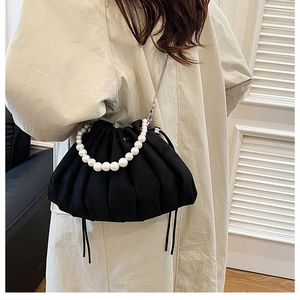 Detail of a black pleated cloud bag with white pearl handle and silver chain strap