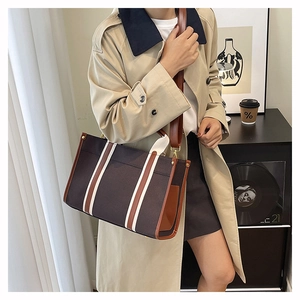 Detail of canvas tote bag with brown leather trim and striped strap on beige coat