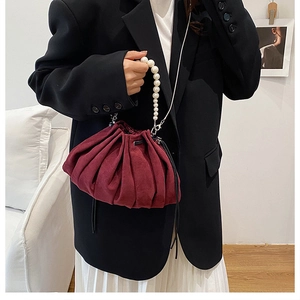 Detail of burgundy pleated bucket bag with large pearl handle and silver shoulder strap