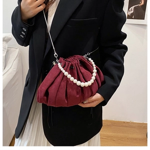 Detail of burgundy ruched drawstring bag with pearl handle and metal chain on model