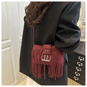 Detail of burgundy suede crossbody bag featuring long fringe and a studded wide strap
