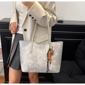 Detail of silver marble texture tote bag with beaded charm on elegant model