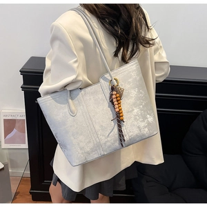 Silver-grey textured tote bag with wood bead tassel shown on a model in a beige suit