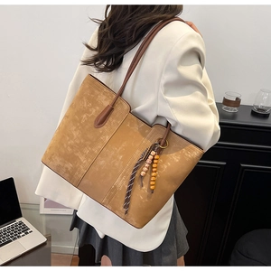 Detail of tan suede tote bag featuring vintage texture and woven tassel pendant