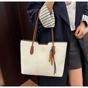 Detail of white tote bag with textured surface and decorative wooden bead tassel accent