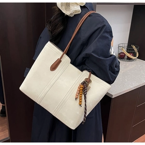 Detailed view of cream leather tote bag featuring vertical stitching and tassel charm