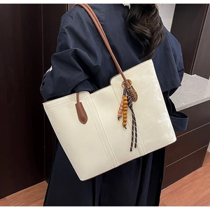 Detailed view of a large cream tote bag with brown handles and a stylish bead charm